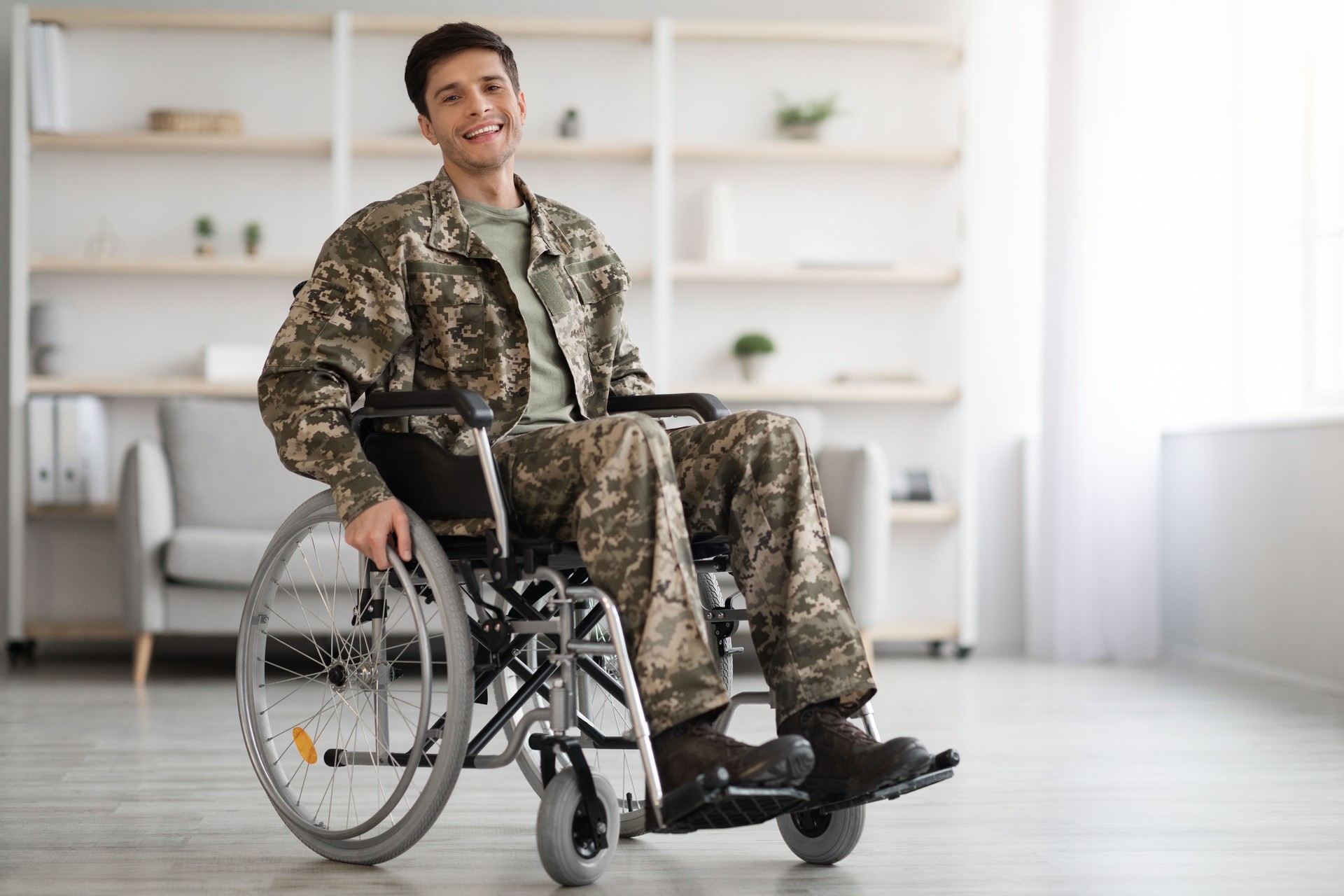 Cheerful young man soldier sitting in wheelchair, home interior